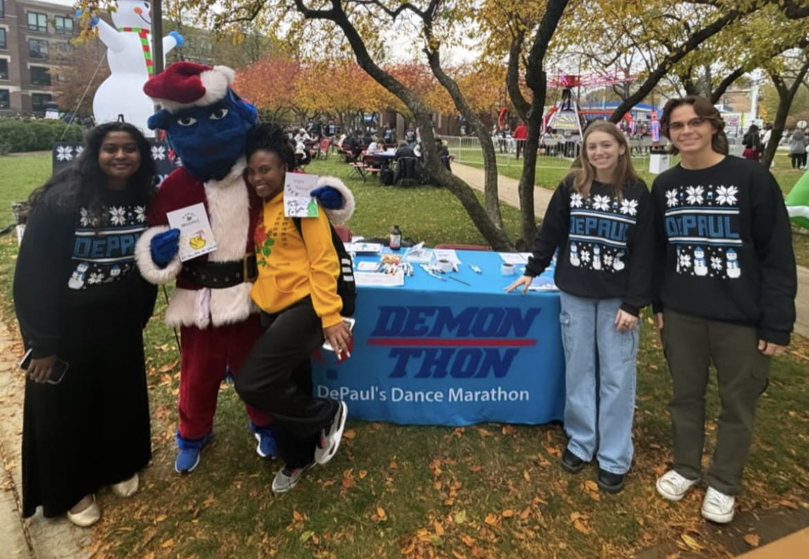  DePaul University mascot DIBS posing with students in front of the DemonTHON table at the DePaul University Ugly Sweater Party.<br />

