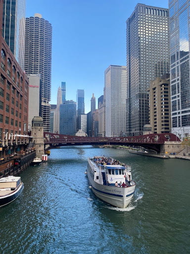 An image of the Chicago River, flanked on either side by skyscrapers that make up the Chicago Skyline. A boat floats on the river toward the photographer.