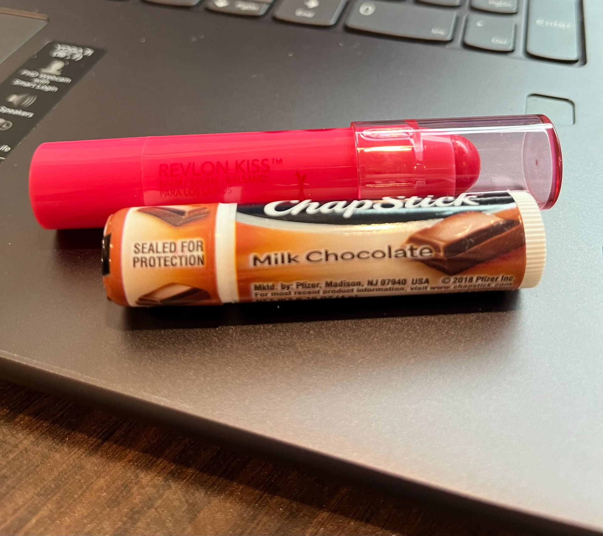 Two chapsticks one in a pink tube the other in a brown resting on a surface. 