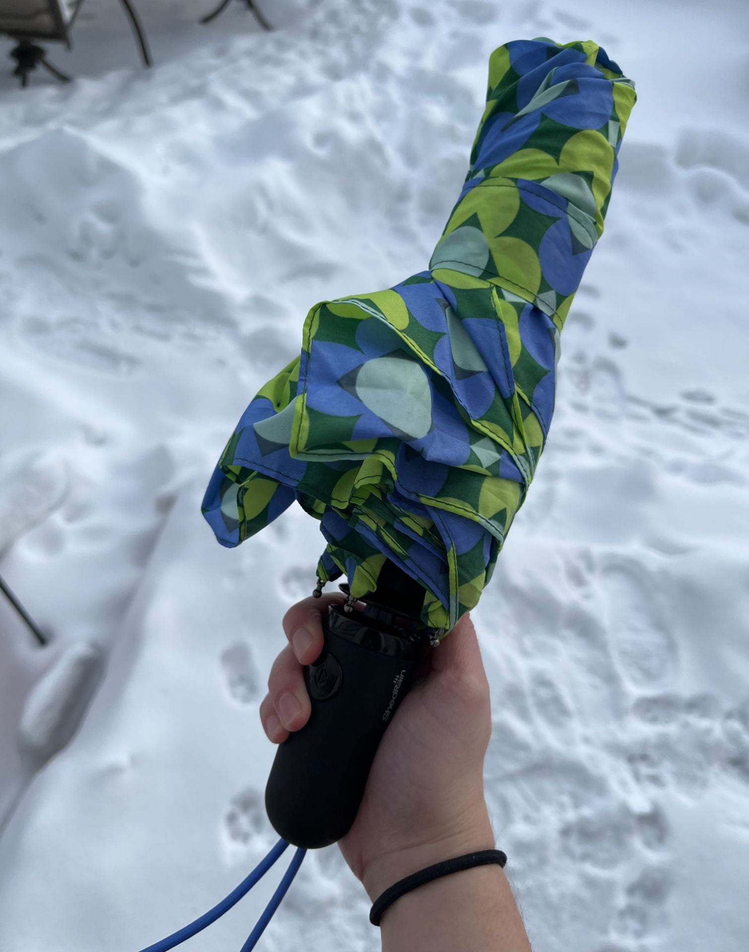 A bright green and blue umbrella with snow as a background. 