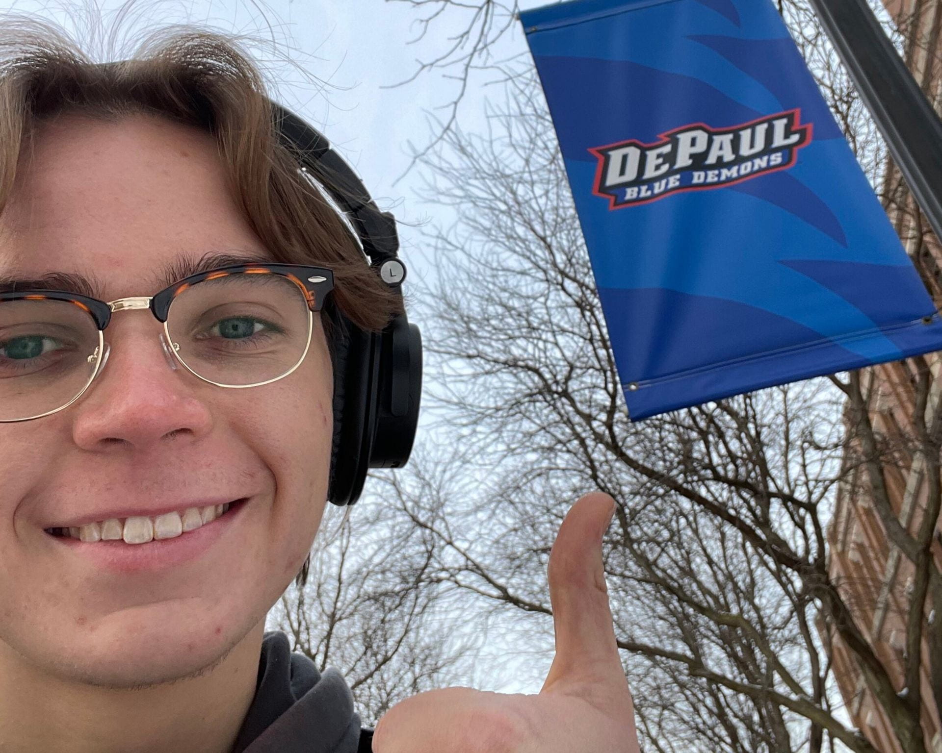 DePaul University student Jeff gives a thumbs up in front of a banner in the DePaul University quad.
