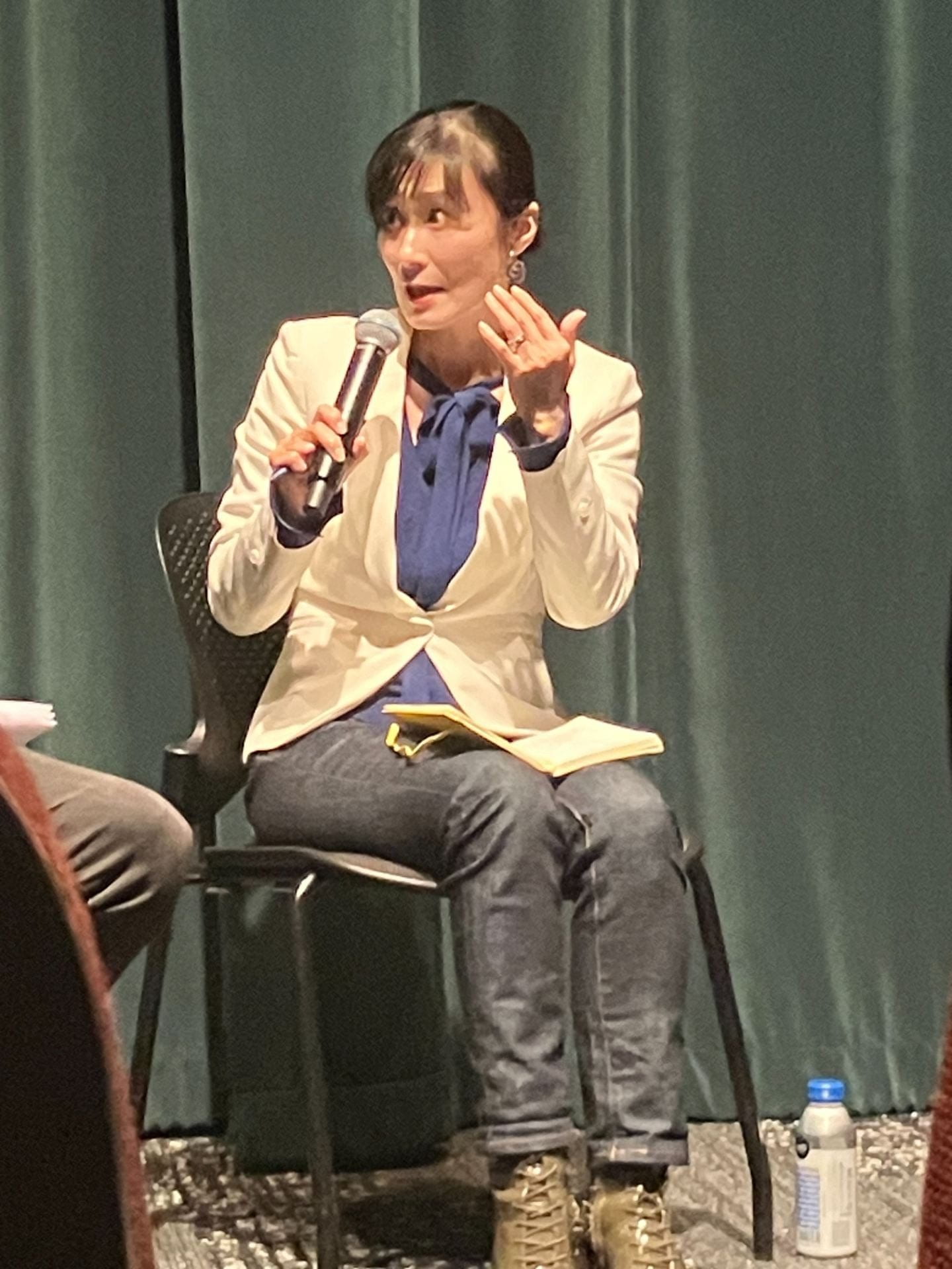 Professor Miyamoto talking during the panel. She wears a white blazer and blue blouse as she emphatically explains a concept to the audience.