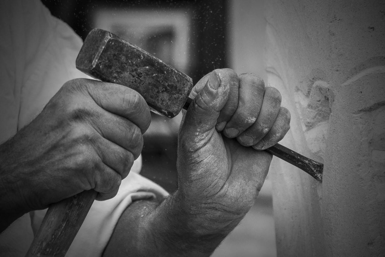 Hands holding a hammer and chisel, depicting a sculptor at work