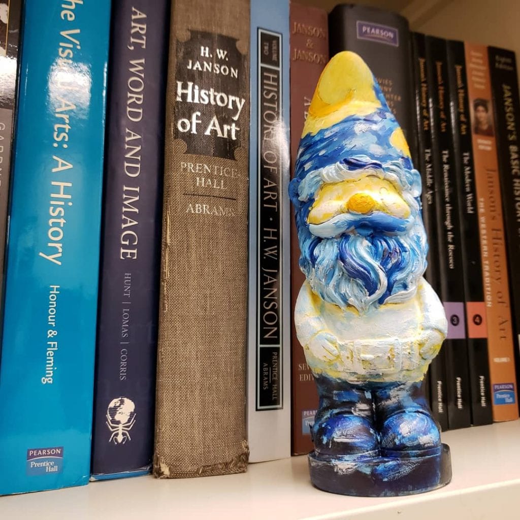 a small garden gnome painted to resemble Vincent van Gogh's Starry Night standing in front of books on a shelf