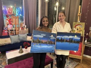 Two women hold up paintings they've made