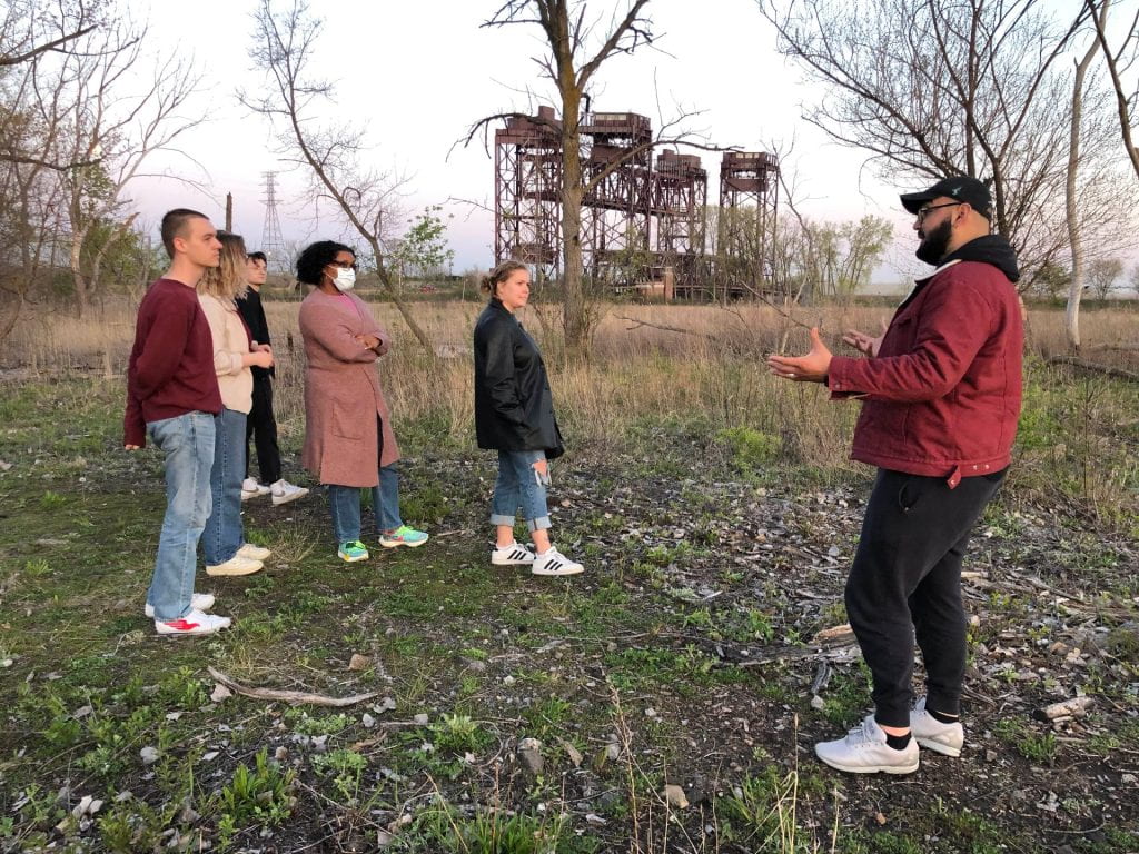 Five DePaul community students stand in a field during late fall listening to a presenter talk about the area. 