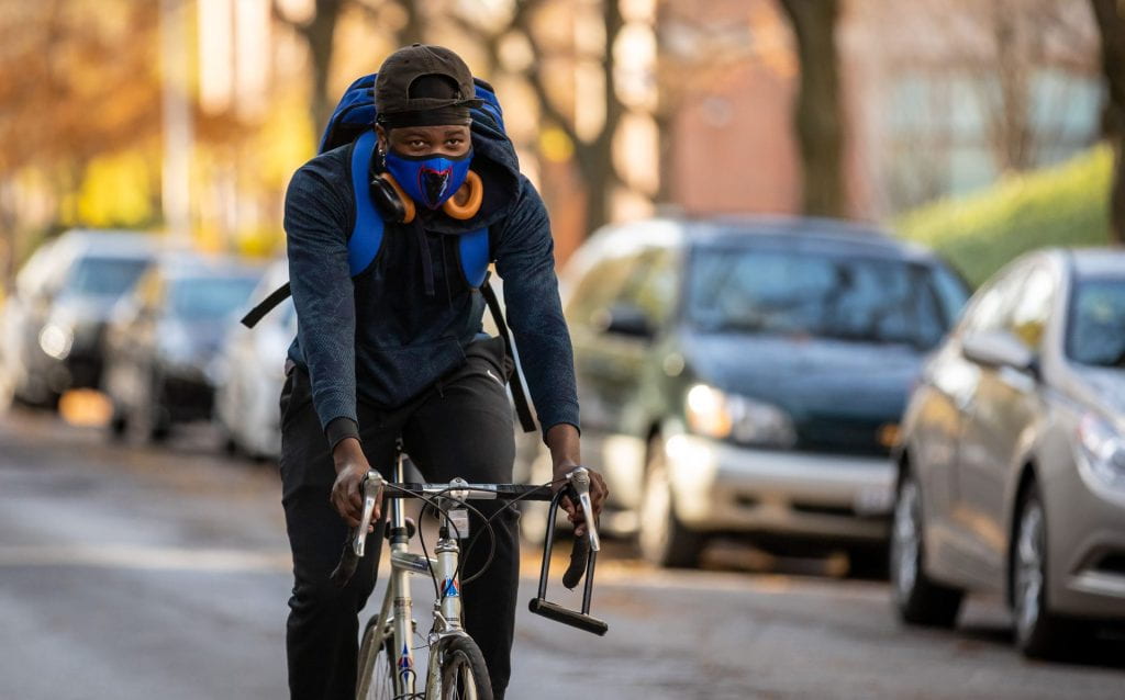 A student wearing a DePaul safety face mask bicycles on campus.